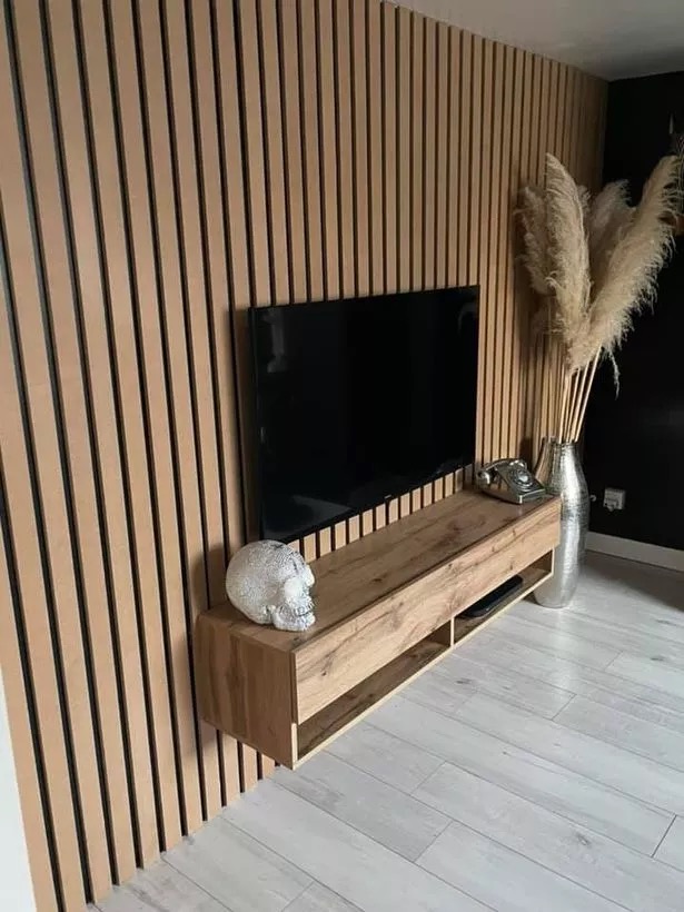 Oak slatted wall panelling with a large TV and ornaments on a cabinet, with pampas grass in a silver vase.