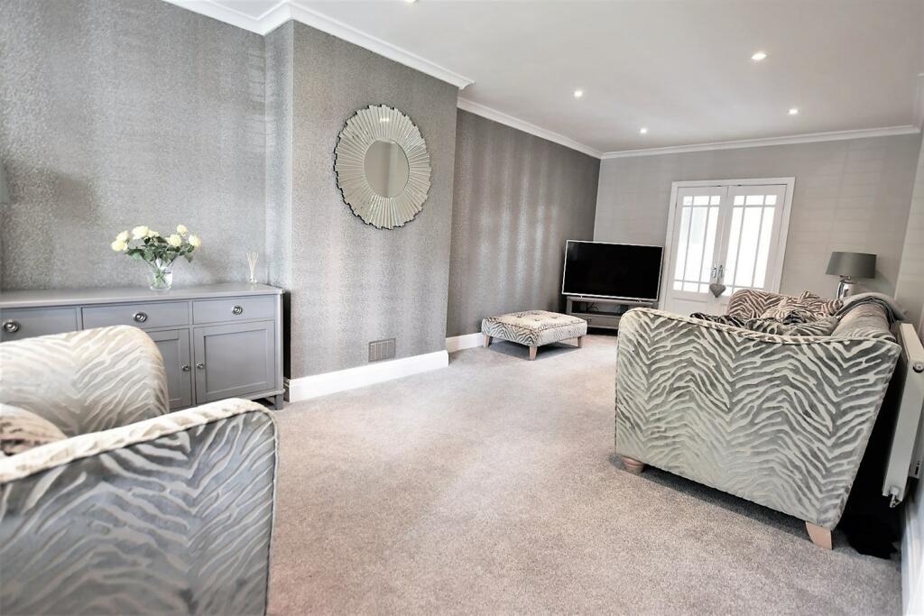 posh front room with nice furnishings and wallpapered walls. Round mirror situated on a chimney wall with a zebra sofa