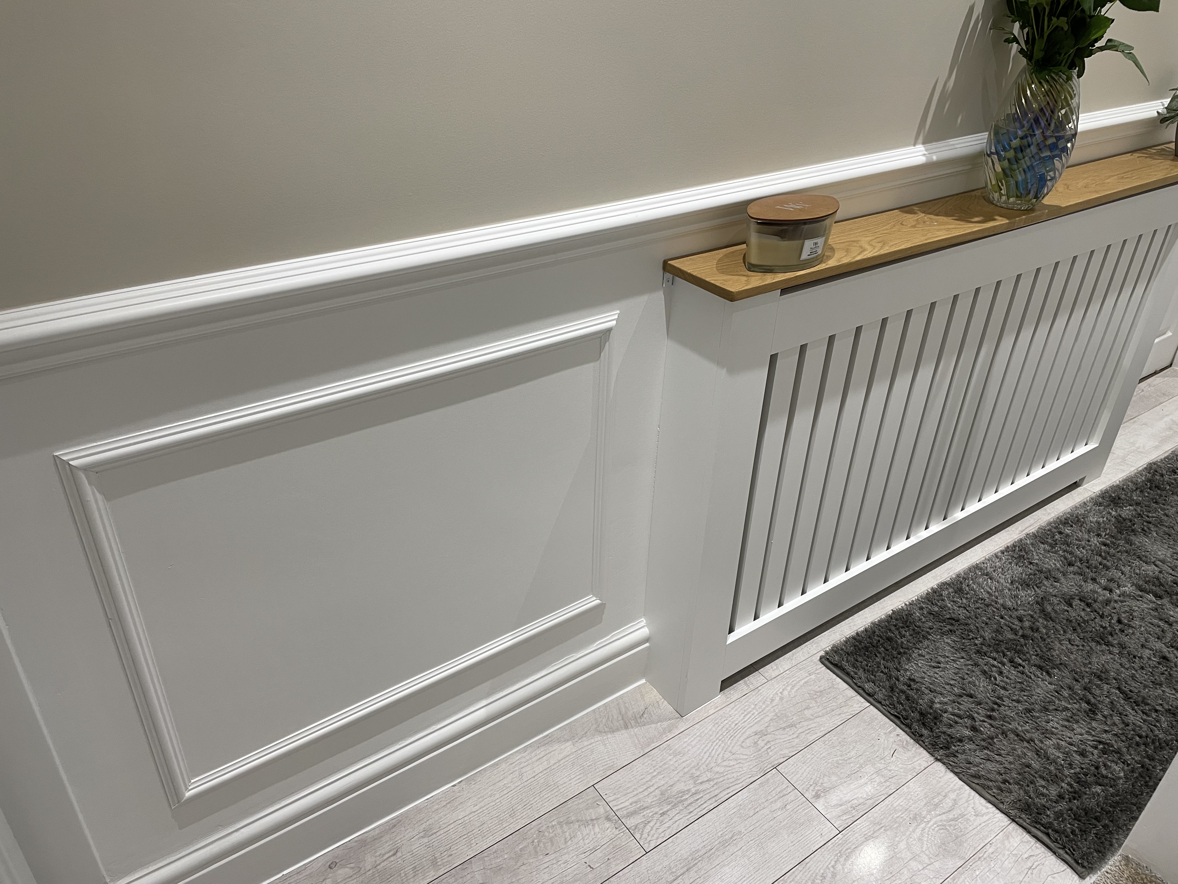 White wall moulding with a dado rail and radiator cover with an oak top. small dark grey rug with light grey laminate flooring