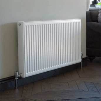 white radiator with chrome fittings on a cream wall with oak parquet flooring.