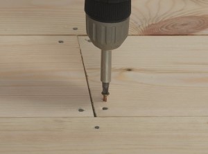 drill putting a screw into pine floorboard.