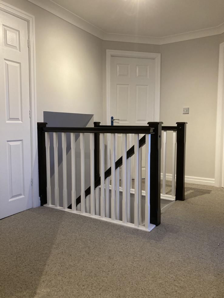 upstairs landing with black hand rail and white spindles, followed by a grey carpet and white doors.