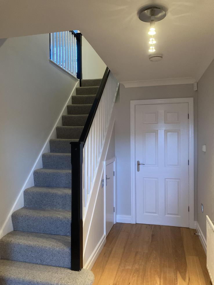 staircase with black hand rail and white spindles with a white door. downstairs hallway