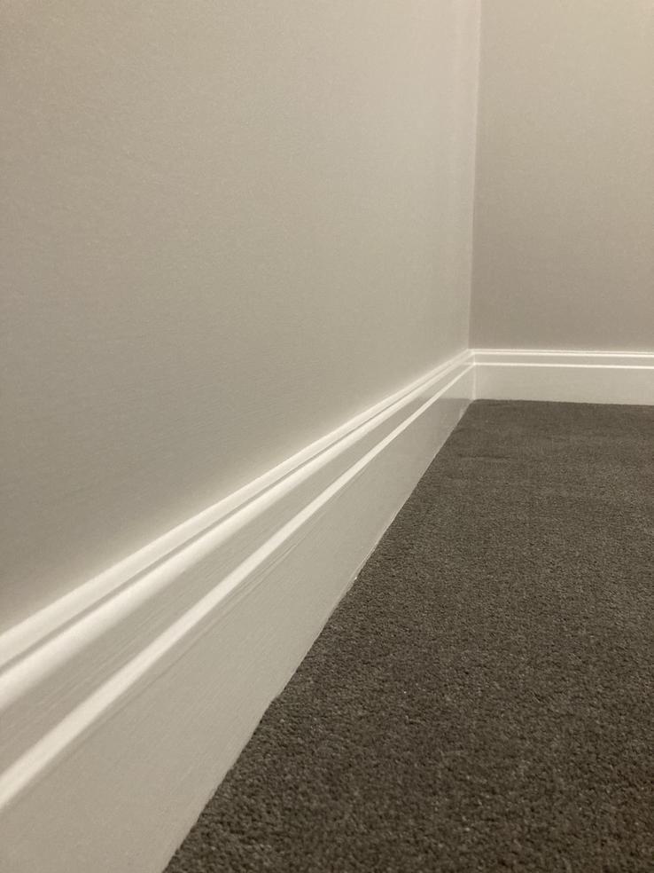close up of white painted skirting board with grey carpet